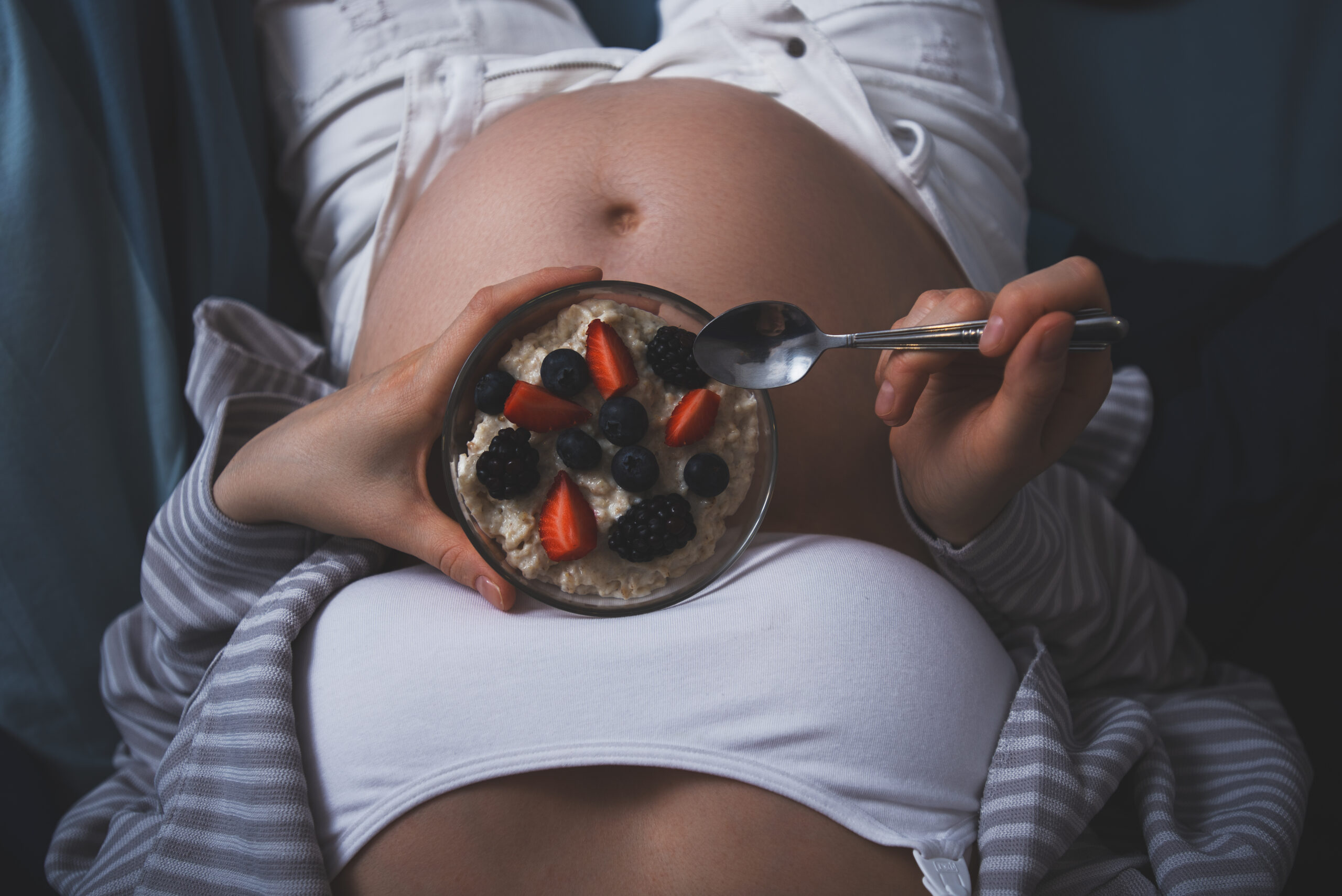 cropped image of pregnant woman in bed with oatmeal with berries, healthy breakfast in bed, healthy pregnancy
