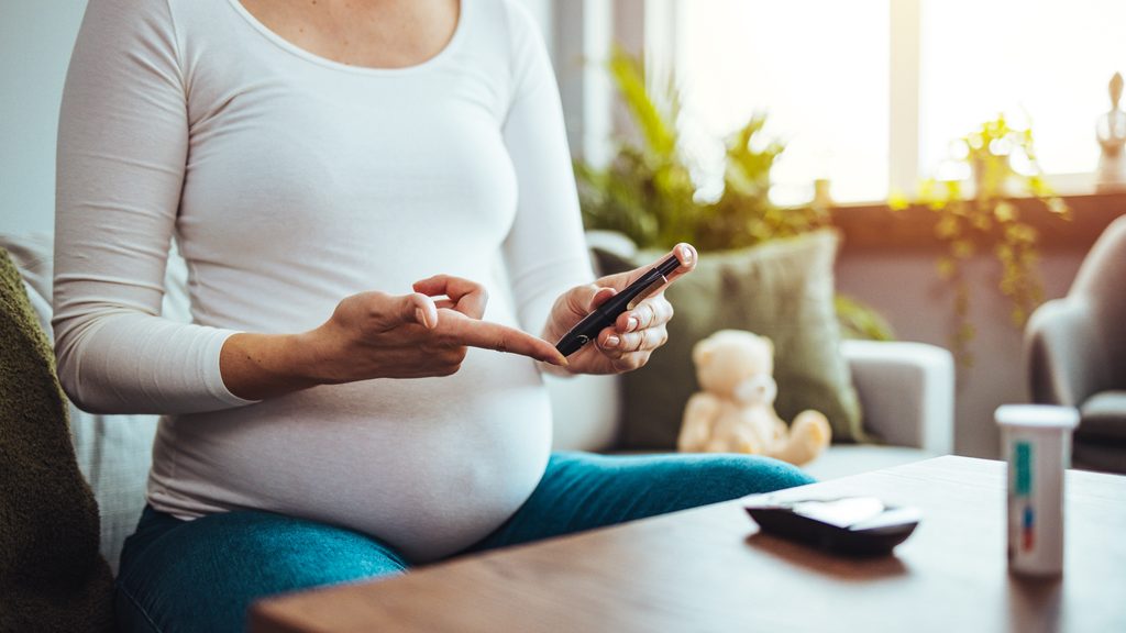 happy pregnant woman with glucometer checking blood sugar level at home. woman testing for high blood sugar. pregnant woman holding device for measuring blood sugar...